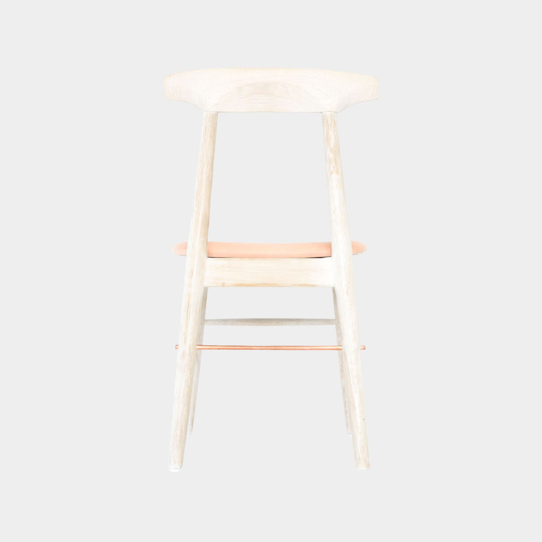 The Earl Home SABLE Dining Chair features a hand-made, bleached oak wooden design with a curved backrest and four legs. Its flat seat exemplifies minimalist elegance, crafted from solid wood for lasting durability. Raw vegtan leather upholstery.