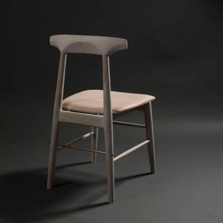 The Earl Home SABLE Dining Chair features a hand-made, bleached oak wooden design with a curved backrest and four legs. Its flat seat exemplifies minimalist elegance, crafted from solid wood for lasting durability. Raw vegtan leather upholstery.