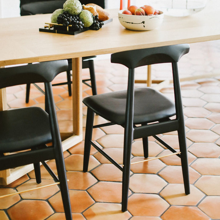 The Earl Home SABLE Dining Chair features a hand-made, ebonized oak or walnut wooden design with a curved backrest and four legs. Its flat seat exemplifies minimalist elegance, crafted from solid wood for lasting durability. Black leather upholstery.