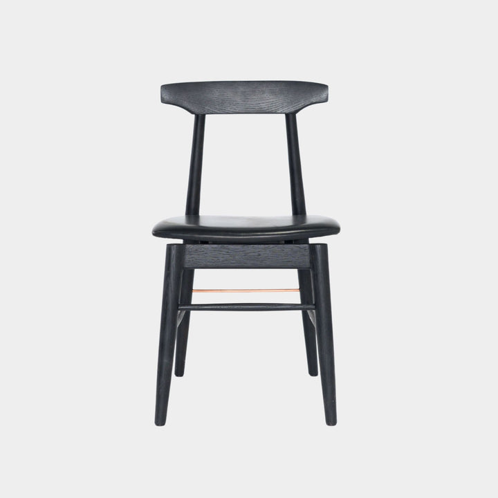 The Earl Home SABLE Dining Chair features a hand-made, ebonized oak wooden design with a curved backrest and four legs. Its flat seat exemplifies minimalist elegance, crafted from solid wood for lasting durability. Black leather upholstery.