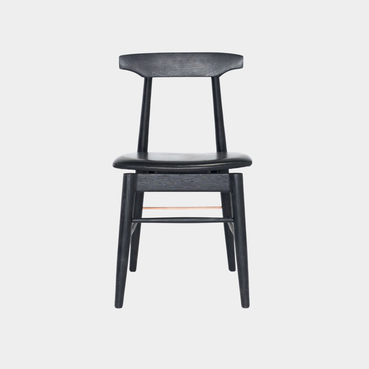 The Earl Home SABLE Dining Chair features a hand-made, ebonized oak wooden design with a curved backrest and four legs. Its flat seat exemplifies minimalist elegance, crafted from solid wood for lasting durability. Black leather upholstery.