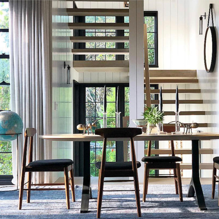 The Earl Home SABLE Dining Chair features a hand-made, walnut wooden design with a curved backrest and four legs. Its flat seat exemplifies minimalist elegance, crafted from solid wood for lasting durability. Black leather upholstery.