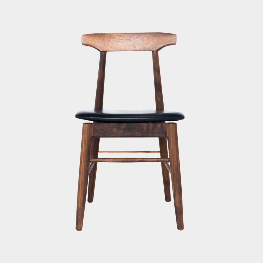 The Earl Home SABLE Dining Chair features a hand-made, walnut wooden design with a curved backrest and four legs. Its flat seat exemplifies minimalist elegance, crafted from solid wood for lasting durability. Black leather upholstery.