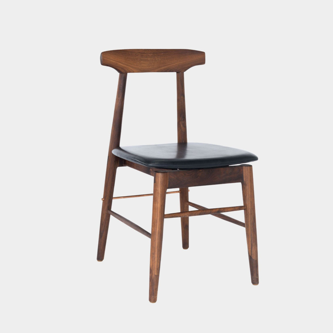 The Earl Home SABLE Dining Chair features a hand-made, walnut wooden design with a curved backrest and four legs. Its flat seat exemplifies minimalist elegance, crafted from solid wood for lasting durability. Black leather upholstery.