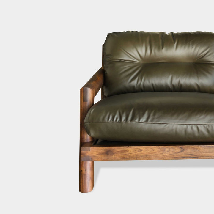 Earl Home's TAMBU Sofa features an American walnut wooden frame with green cushions and three backrests against a minimalist background. Handmade to order, it seamlessly blends elegance with bespoke craftsmanship in its striking design.