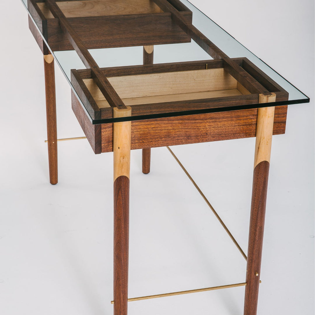 The WRITING Desk by Earl Home is an elegant glass desk with walnut and maple spliced wooden legs and a tempered glass top, Accompanied by a matching wooden chair. You can customize it to create your perfect workspace.