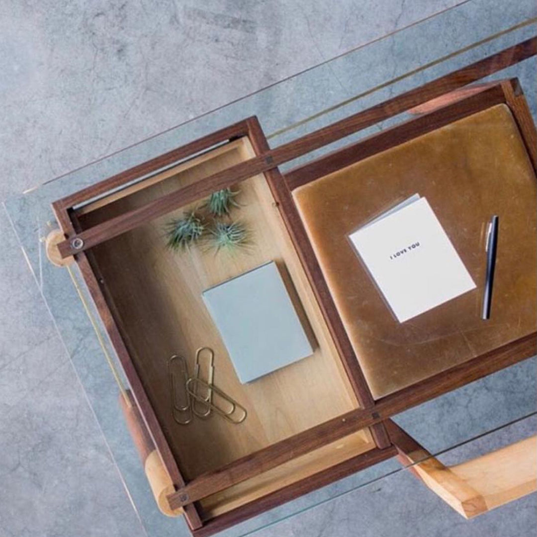 The WRITING Desk by Earl Home is an elegant glass desk with walnut and maple spliced wooden legs and a tempered glass top, Accompanied by a matching wooden chair. You can customize it to create your perfect workspace.