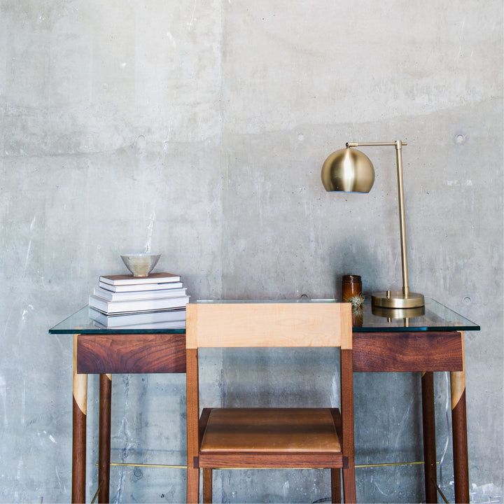 The WRITING Desk by Earl Home is an elegant glass desk with walnut and maple spliced wooden legs and a tempered glass top, Accompanied by a matching wooden chair. You can customize it to create your perfect workspace.