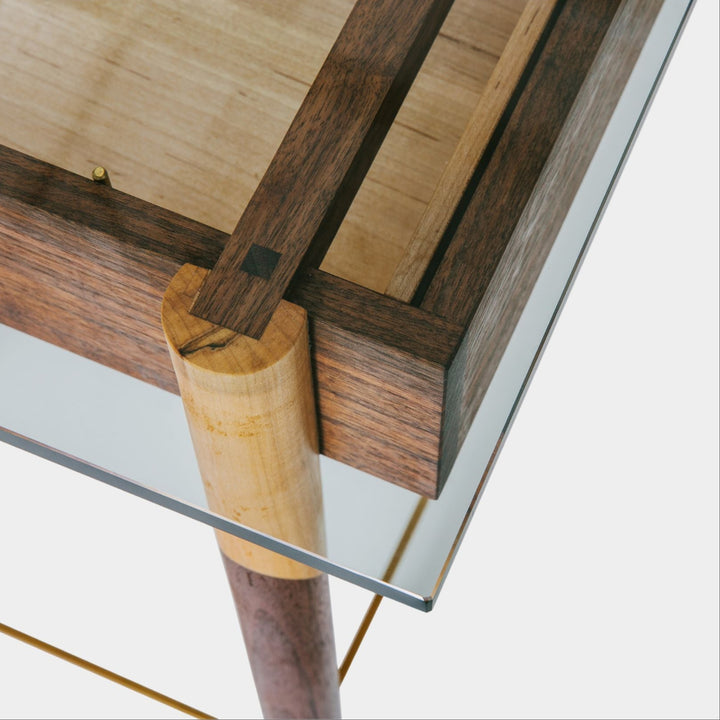 The WRITING Desk by Earl Home is an elegant glass desk with walnut and maple spliced wooden legs and a tempered glass top, Accompanied by a matching wooden chair. You can customize it to create your perfect workspace.
