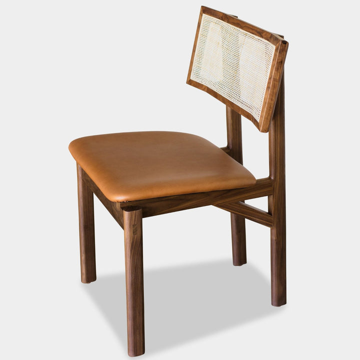 The KUNAI Dining Chair by Earl Home is handcrafted to order, featuring a solid walnut frame, brown camel leather seat, and woven cane backrest.